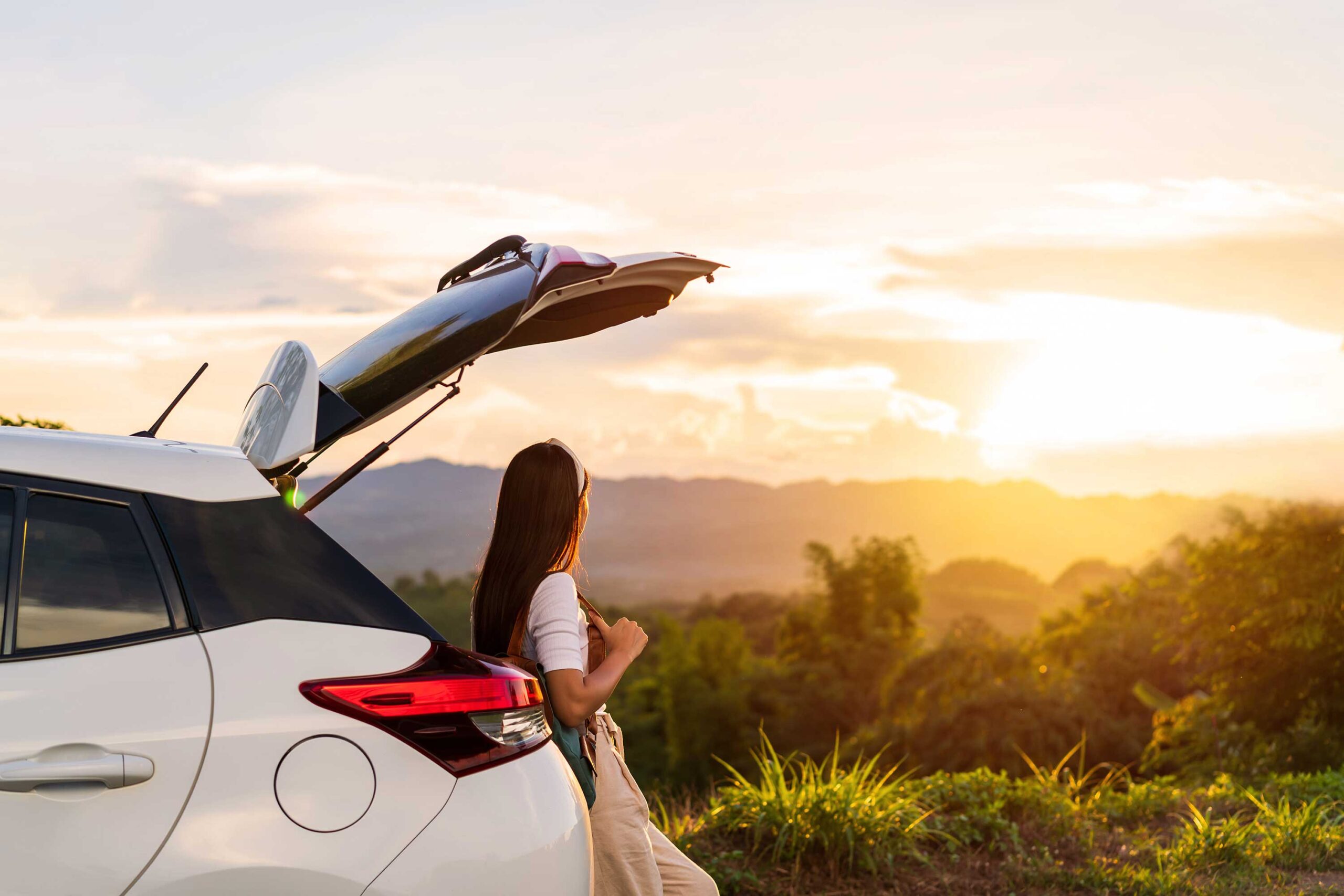 Woman relaxing by car at sunset in nature.
